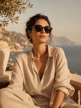 Woman wearing sunglasses with a scenic background of mountains and sea.